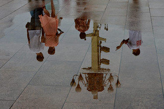 Uma poça na praça de Tiananmen, em Pequim, refletindo chineses sendo vigiados por câmeras de vigilância anexadas a um poste de iluminação em estilo tradicional