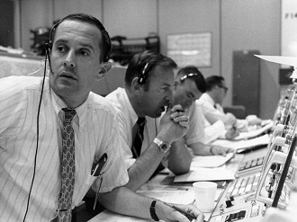 CAPCOM Charlie Duke (em primeiro plano) com o comandante reserva Jim Lovell (ao centro) durante o pouso tenso do Apollo 11