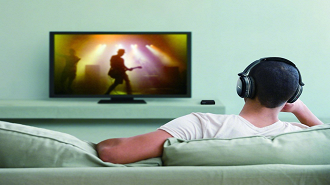 Imagem ilustrativa de pessoa assistindo a TV com fones de ouvido sem fio Bluetooth. Fonte: improb