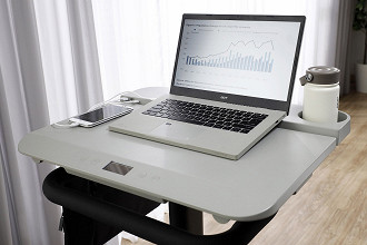 A mesa tem tela LCD, controles de ajuste, suporte para notebook, bolsa, garrafas e três portas USB